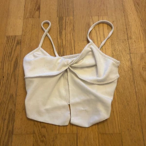 Vit bandeau tubtopp med knut - Snygg vit bandeau tubtopp med smala axelband och knutdetalj framtill. Toppen har en liten slits i mitten nedtill och är perfekt för varma dagar. Enkel och stilren design som passar till många outfits.