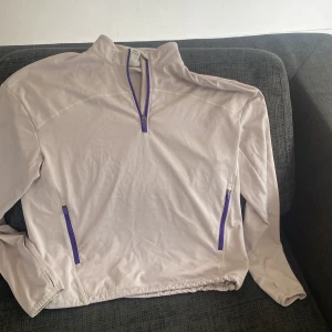 Ljuslila half zip tröja från H&M Move - Sportig ljuslila långärmad tröja från H&M Move med lila detaljer och half zip framtill. Tröjan har två fickor med dragkedja och är tillverkad i mjukt syntetmaterial, perfekt för träning eller chill. Snygg och enkel design med hög krage.