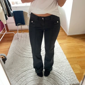 Svarta bootcut byxor med fickor - Säljer ett par svarta byxor med bootcut-snitt och snygga fickdetaljer framtill. Byxorna har låg midja och markerade sömmar som ger en cool look. Perfekta för dig som gillar en klassisk men trendig stil.