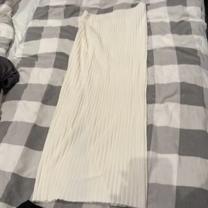 Vit ribbad långkjol från Gina Tricot - Säljer en snygg vit långkjol från Gina Tricot i ribbat material. Kjolen har en rak passform och en slits på sidan som ger en chill vibe. Perfekt att styla med sneakers eller boots för en trendig look.