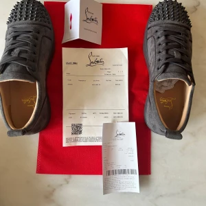 Christian Louboutin grå mocka sneakers - Snygga grå sneakers från Christian Louboutin i mocka med ikoniska röda sulor och svarta nitar på tån. Skorna har rund tå, snörning och en cool streetstil vibe. Perfekta för dig som vill sticka ut med exklusiva detaljer och lyxig känsla. Priset är inte hugget i sten hör av dig vid minsta lilla fundering !