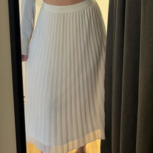 Vit plisserad långkjol - Säljer en snygg vit plisserad långkjol med elastisk midja. Kjolen har ett luftigt och flowy tyg som ger en stilren och fräsch look. Sitter mycket smickrande på! Köpt på Veromoda.