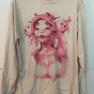 Melanie Martinez Portals tröja - Beige långärmad tröja från Melanie Martinez Portals tour med stor rosa tryck fram och turnédatum bak. Köpt på stockholm konserten 2023! enbart använd ett fåtal gånger💕är lite liten i storleken så skulle nog säga att det är mer som en L