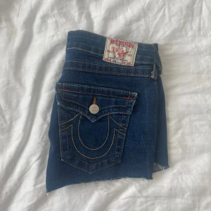 True Religion jeansshorts blå, stl 31 - Snygga blå jeansshorts från True Religion med ikoniska bakfickor och kontrastsömmar. Klassisk femficksmodell, låg midja och råa. Made in USA. Köpte av en tjej på Vinted men de var tyvärr för stora, klippte också om de lite så att de blev kortare. Om ni har frågor är det bara att fråga! 