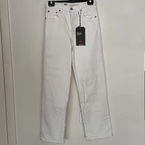 Levi's Ribcage Straight Ankle vita jeans - Snygga vita Levi's Ribcage Straight Ankle jeans med superhög midja och raka ben. Klassisk femficksmodell med silverfärgade knappar och nitar, samt brunt läderpatch bak. Perfekta för dig som gillar en clean och stilren look.
