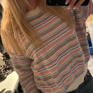 Randig pastellfärgad stickad tröja - Superfin stickad tröja i pastelliga färger med randigt mönster i rosa, blått, vitt och beige. Tröjan har rund halsringning, långa ärmar och ribbade muddar. Perfekt för dig som gillar en mysig och färgglad stil.