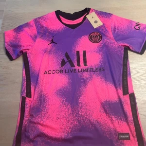 PSG Neymar Jr 10 fotbollströja rosa/lila - Snygg PSG fotbollströja med Neymar Jr och nummer 10 på ryggen. Tröjan har ett unikt rosa och lila mönster, svarta detaljer och loggor. Tillverkad i lätt och ventilerande material, perfekt för match eller träning. Jordan-logga på bröstet och Paris-märke.