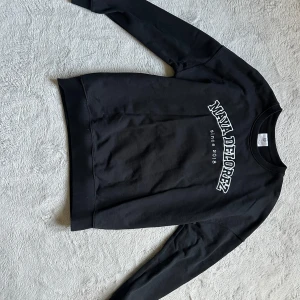 Svart sweatshirt Maya Delorez - Svart sweatshirt från Maya Delorez med vit broderad logga och text på bröstet. Klassisk rund halsringning och långa ärmar. Skön passform och tillverkad i mjuk bomullsmix, perfekt för chill dagar eller till stallet. Aldrig använd 