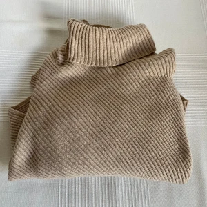 Beige ribbad poloponcho - En poncho från GinaTricot i en varm beige färg. Ponchon har en lösare polokrage upptill. Återkom gärna vid fler bilder. 