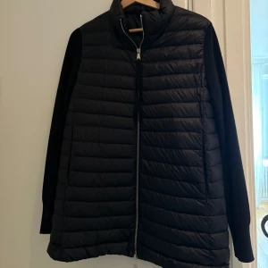 Svart Moncler cardigan jacka  - Snygg svart cardigan jacka från Moncler med quiltad front och stickade ärmar. Jackan har hög krage, hel dragkedja och Moncler-logga på ärmen. Perfekt för dig som vill ha en stilren och sportig look med premiumkänsla. Storlek M. Pris kan diskuteras vid snabb affär.