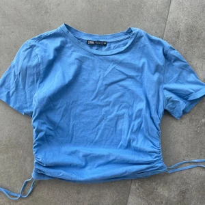 Blå croppad T-shirt från Zara - Snygg blå croppad T-shirt från Zara med dragsko på sidorna. Storlek M men passar även S och XS.