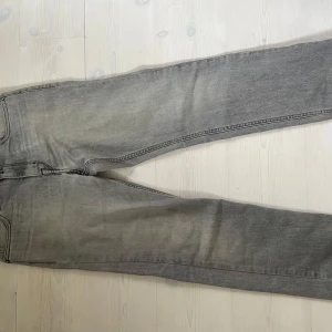 Replay grå jeans Thad modell - Snygga grå jeans från Replay i Thad-modell. Jeansen har klassisk femficksdesign, raka ben och diskreta sömmar på bakfickorna. Tillverkade i mjukt bomullsmaterial med en lätt tvättad look. Perfekta för dig som gillar stilrena och avslappnade jeans.