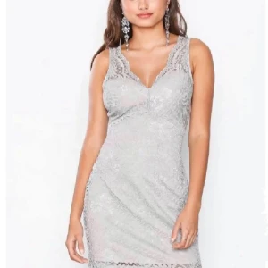 Ljusgrå spetsklänning med v-ringning - Superfin ljusgrå kortklänning från med v-ringning fram och bak. Klänningen är ärmlös och täckt av detaljerad spets med blommigt mönster. Perfekt för dig som vill sticka ut med en elegant look