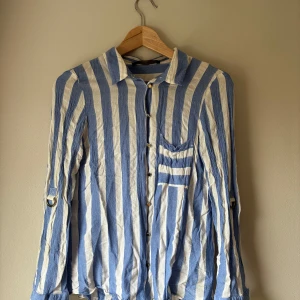 Blåvit randig skjorta från Zara Basic - Snygg blå och vit randig skjorta från Zara Basic i storlek L (upplevs som liten i storlek - passar snarare S/liten M). Skjortan har långa ärmar som kan kavlas upp och fästas, bröstficka och klassisk krage. Tillverkad i ett luftigt linneliknande material som passar perfekt för en avslappnad stil.