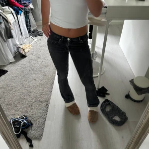Svarta bootcut jeans med låg midja - Säljer ett par svarta jeans med snygg bootcut och låg midja. Jeansen har klassiska fem fickor, vita sömmar och är i stretchigt denimtyg som sitter tajt över låren och släpper ut vid anklarna. Perfekta för dig som gillar en stilren och trendig look.