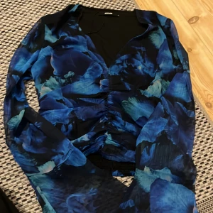 Blommig blå blus från BikBok - Säljer en snygg blommig blus från BikBok i olika blå nyanser. Blusen har v-ringning, långa ärmar och rynkade detaljer framtill som ger en cool look. Perfekt för dig som vill sticka ut med ett unikt mönster och fräscha färger.