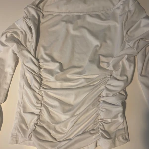 Vit  långärmad topp med snörning - Trendig  långärmad topp med snygga rynkade detaljer och snörning längs sidorna. Mjuk och stretchig känsla, perfekt att styla med jeans eller kjol. ☺️