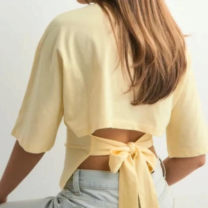 Gul  topp med knyt från Nelly - Superfin ljusgul topp från Nelly med korta ärmar och snygg knytning i ryggen. Använts en gång.