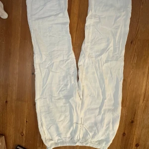 Vita linnebyxor med resår - Säljer ett par vita linnebyxor med avslappnad passform och resår i benslut. Byxorna har en luftig känsla och är perfekta för varma dagar. De har en enkel design utan synliga fickor eller detaljer, vilket gör dem lätta att matcha med olika stilar.