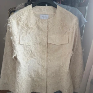 Beige overshirt från Stockh LM Studio - Säljer en beige overshirt från Stockh LM Studio i storlek S. Jackan har en cool, texturerad yta med fransiga detaljer och två stora bröstfickor. Rak passform och rund halsringning, perfekt för dig som gillar en unik och trendig look. Har en liten sminkfläck och vågar inte tvätta bort den därav priset!