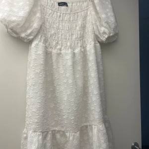 Vit blommig kortklänning från LMTD - Superfin vit kortklänning från LMTD med puffärmar och broderade blommor. Klänningen har smock upptill och volang nertill, vilket ger en söt och luftig känsla. Perfekt för sommarens alla tillfällen!