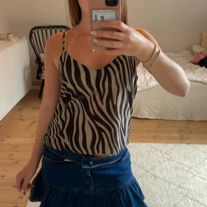 Zebramönstrad linnetopp från Bershka - Säljer en snygg zebramönstrad linnetopp från Bershka i storlek S. Toppen har tunna axelband, v-ringning och är i svart och beige. Djupare i ryggen.