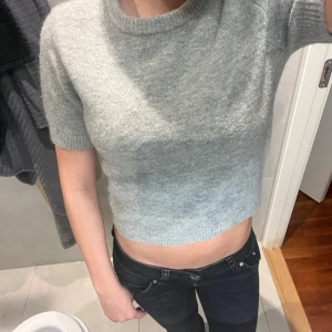 Grå croppad stickad tröja från Zara - Supermjuk och croppad grå stickad tröja från Zara. Tröjan har korta ärmar, rund halsringning och ribbade kanter.