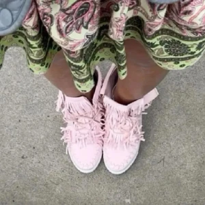 Rosa mockasneakers med fransar - Unika sneakers i ljusrosa mocka med coola fransdetaljer runt skaftet och framtill. Skorna har snörning och en platt sula med dekorativa sömmar. Perfekta för dig som vill sticka ut med en boho-inspirerad stil.