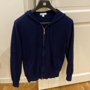 Mörkblå hoodie i kashmir från Barlucio - Mysig mörkblå zip hoodie från Barlucio i mjuk kashmir. Tröjan har dragkedja framtill, huva med snörning och två fickor. Perfekt för dig som gillar en stilren och chill look med premiumkänsla. Den är något nopprig men inget som ej går att fixa.