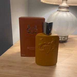 Parfums de Marly Althair 125 ml - Säljer en lyxig Althaïr Eau de Parfum från Parfums de Marly. Flaskan är i en elegant guldfärg med en silverfärgad kork och har en stilren design med reliefmönster. Förpackningen är i matchande färg och rymmer 125 ml av denna exklusiva doft.