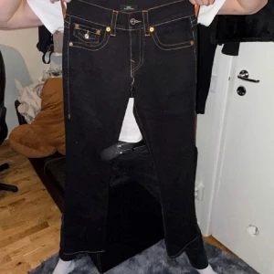 Svarta jeans från True Religion - Snygga svarta straight leg jeans från True Religion med orange sömmar och klassiska femficksdesign. Skick 10/10 oanvända bara testade en gång. Storlek W28, längd 116 cm. Perfekta för en stilren look.