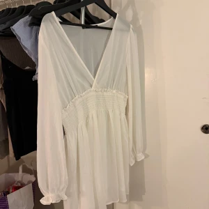 Vit klänning från 157 - Säljer en söt vit klänning från 157 med v-ringning och långa ärmar. Klänningen har en smockdetalj i midjan som ger en fin passform. Perfekt för en stilren look!😍