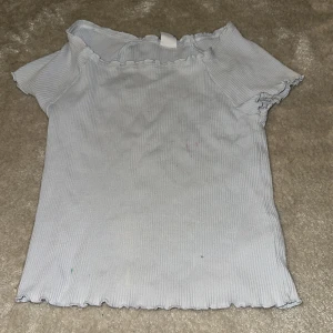 Ljusblå ribbad topp från Lindex - Säljer en ljusblå ribbad topp från Lindex för barn. Toppen har korta ärmar och en vågig kant vid ärmslut och nederkant. Perfekt för en avslappnad stil. 💙