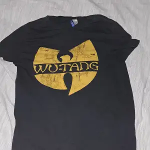 Cool svart t-shirt med stort gult Wu-Tang Clan-logotyptryck på framsidan. Perfekt för fans av hiphop och streetwear. T-shirten har en klassisk passform och är kortärmad, vilket gör den bekväm för vardagsbruk.