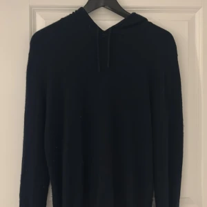 Svart cashmere hoodie från Sagless - Säljer en stilren svart hoodie från Sagless i mjuk cashmere. Perfekt för kyliga dagar med sin bekväma passform och klassiska design. Huvan har snörning för justering. Ett måste i garderoben för den som älskar komfort och stil.