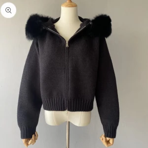 Svart stickad jacka med pälshuva - Snygg svart stickad jacka från Fur Stockholm med dragkedja och en mysig huva kantad med svart äkta päls. Jackan har långa ärmar och ribbade muddar vid ärmslut och nederkant. Perfekt för alla dagar! Helt ny oanvänd med alla etiketter kvar, köpt för ca 2000kr 