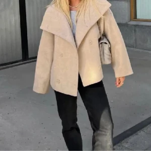 Beige kappa med bred krage - Snygg beige kappa med bred krage och dubbelknäppning. Perfekt för kyligare dagar med sin stilrena design och bekväma passform. Ett måste i garderoben för den som vill ha både stil och komfort.