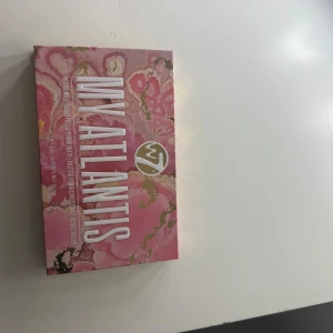 Ögonskuggspalett W7 Atlantis - Snygg ögonskuggspalett från W7 med namnet Atlantis. Innehåller 18 olika nyanser i både matta och skimrande toner. Perfekt för att skapa både vardagliga och festliga looks. Paletten har en inbyggd spegel och en dubbelsidig borste för enkel applicering.