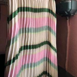 Randig plisserad kjol - Snygg plisserad kjol med randigt mönster i rosa, grönt och vitt. Perfekt för en färgglad look. Kjolen har en elastisk midja för bekväm passform.