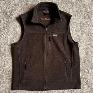 Patagonia väst - Säljer en svart fleeceväst från Patagonia med dragkedja framtill och två praktiska fickor. Västen har en broderad logga på bröstet och en hög krage för extra värme. Perfekt nu till våren! Storlek L