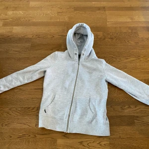 Grå hoodie från superdry| strl 170  - Säljer en stilren grå hoodie med dragkedja och huva. Tröjan har långa ärmar och praktiska fickor framtill. den har inte snören i men kan läggas till på egen hand.
