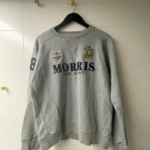 Grå sweatshirt från Morris - Säljer en grå sweatshirt från Morris med tryck på framsidan och siffran 8 på ärmen. Tröjan har långa ärmar och ribbade muddar vid ärmslut och nederkant. Perfekt för en avslappnad stil.