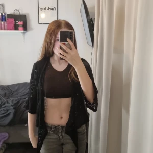 Svart spetsbolero från Elitzia - Säljer en elegant svart spetsbolero från Elitzia. Den har korta ärmar och en öppen design som passar perfekt över en topp eller klänning. Perfekt för att ge en extra touch till din outfit.