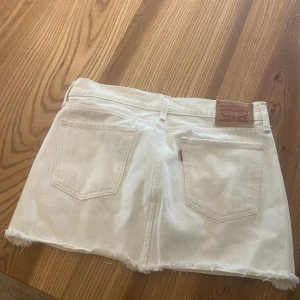 Kort Vit jeanskjol från Levi's❤️ - Snygg vit low waist jeans kjol från Levi's med fransiga kanter och klassisk femficksdesign. Perfekta för en avslappnad sommarlook. Den är vintage och säljs då den inte kommer till andvänding längre❤️skriv för mer frågor och bilder och bud❤️