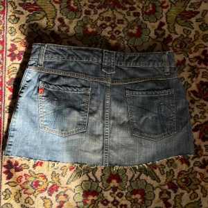 lågmidjad jeanskjol  -  kort lågmidjad jeanskjol från 2000s med snygga broderier på bakfickan.                midjemått rakt av: 39cm Längd: 32cm 