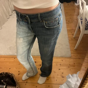 Jean från Tommy Hilfiger - Coola och unika jeans från Tommy Hilfiger med en unik tvåfärgad design. Ena benet är mörkblått och det andra ljusblått. Jeansen har en straight/bootcut passform och klassiska femficksdetaljer. 💕Ytterbensmått 102 cm Innerbensmått 81 cm Midjemått 41 cm rakt över