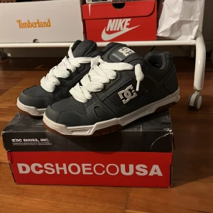 Grå sneakers från DC Shoes - Snygga gråa sneakers från DC Shoes med vit sula och breda vita snören. Perfekta för en avslappnad stil. DC-loggan syns tydligt på sidan av skorna. Bra till sommaren, våren, får även med original snören 