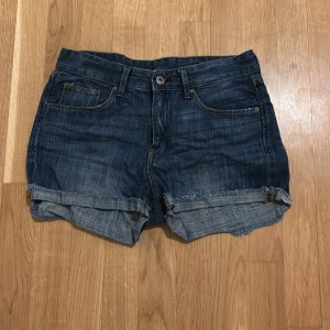 Mörkblå jeansshorts från H&M - Säljer ett par mörkblå jeansshorts från H&M. De har en klassisk femficksdesign och är uppvikta vid bensluten för en avslappnad look. Perfekta för varma sommardagar!
