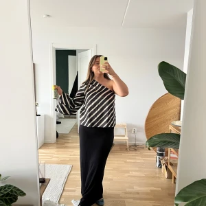 Svartvit randig oneshoulder topp - Snygg svartvit randig oneshoulder topp med vida ärmar. Perfekt för en stilren look med en unik touch. Materialet känns mjukt och bekvämt mot huden.