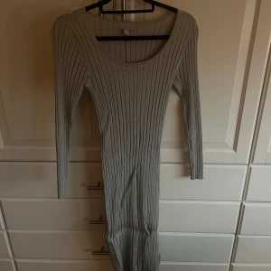Grå ribbad klänning - Snygg grå ribbad klänning med lång ärm och en figurnära passform. Perfekt för en stilren look. Klänningen har en rund halsringning och är gjord i ett mjukt material.